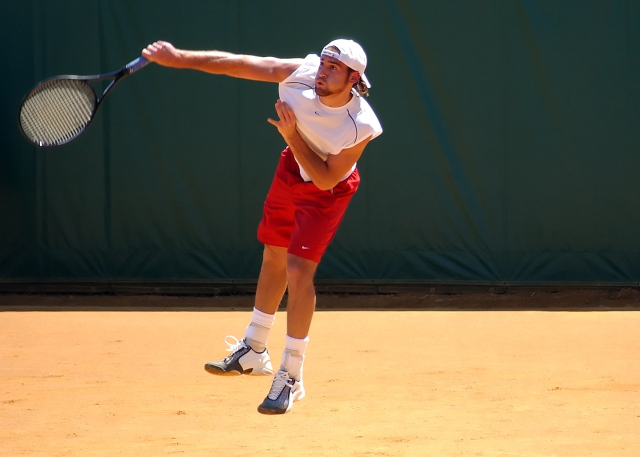 A tennis player in action on a clay court, swinging a racket.
