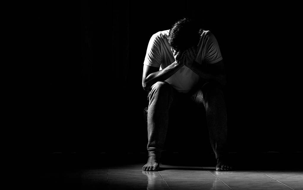 A person sitting alone in darkness, head bowed in contemplation.
