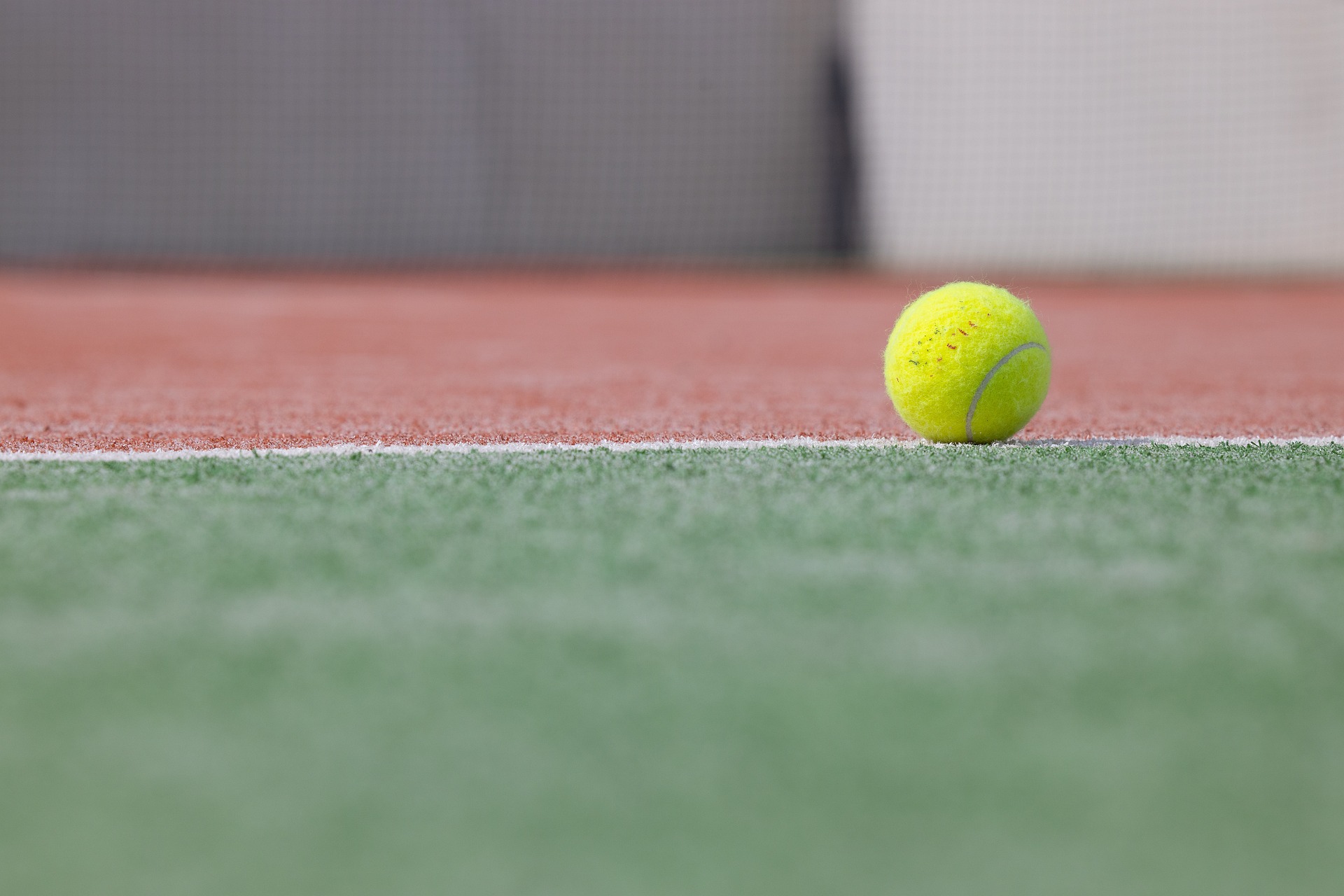A tennis ball resting on a green court near the baseline.