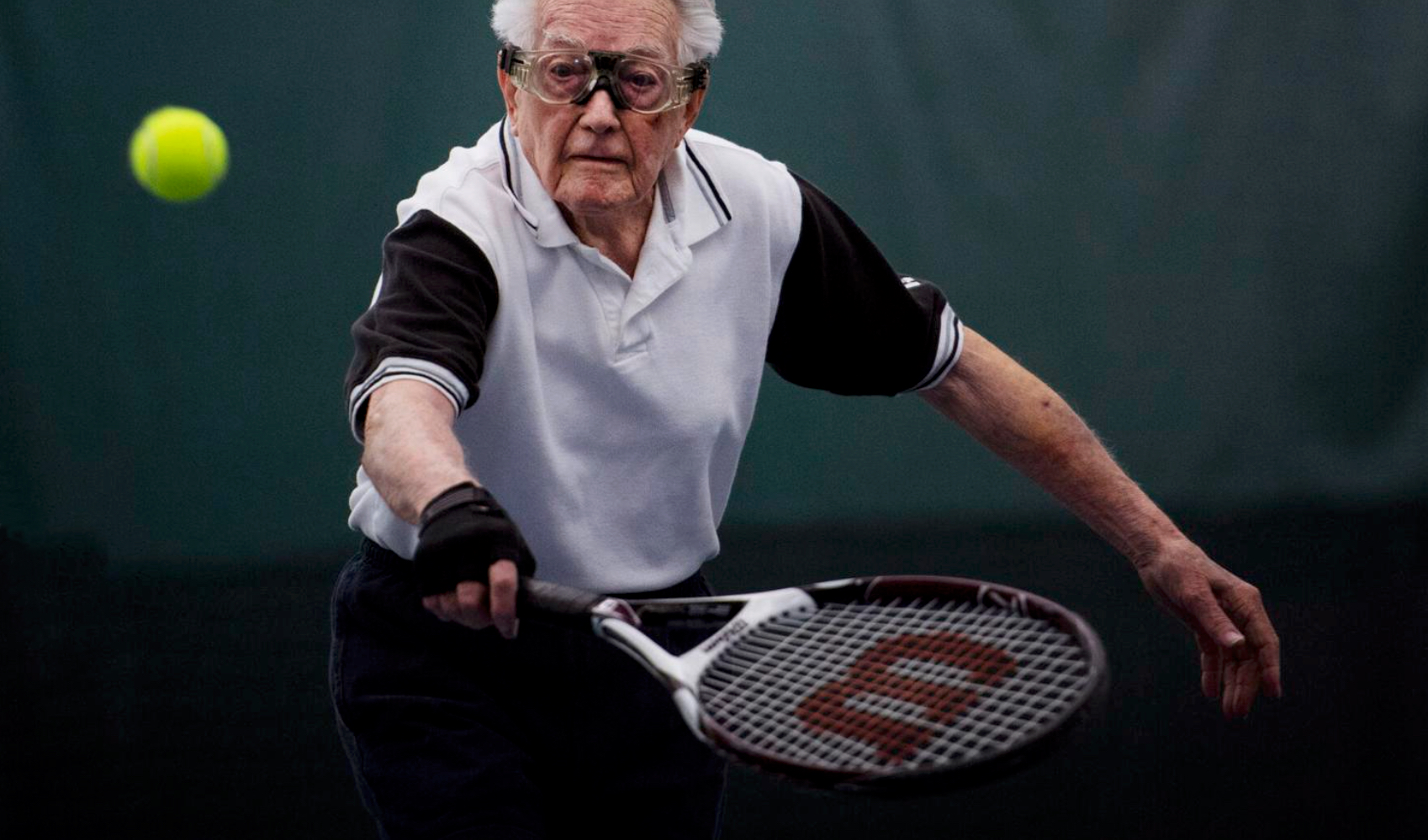 Elderly man playing tennis with focus and determination.