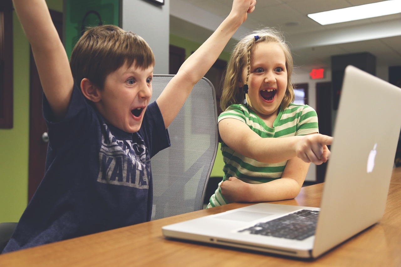 Two kids excitedly cheering at a laptop screen.