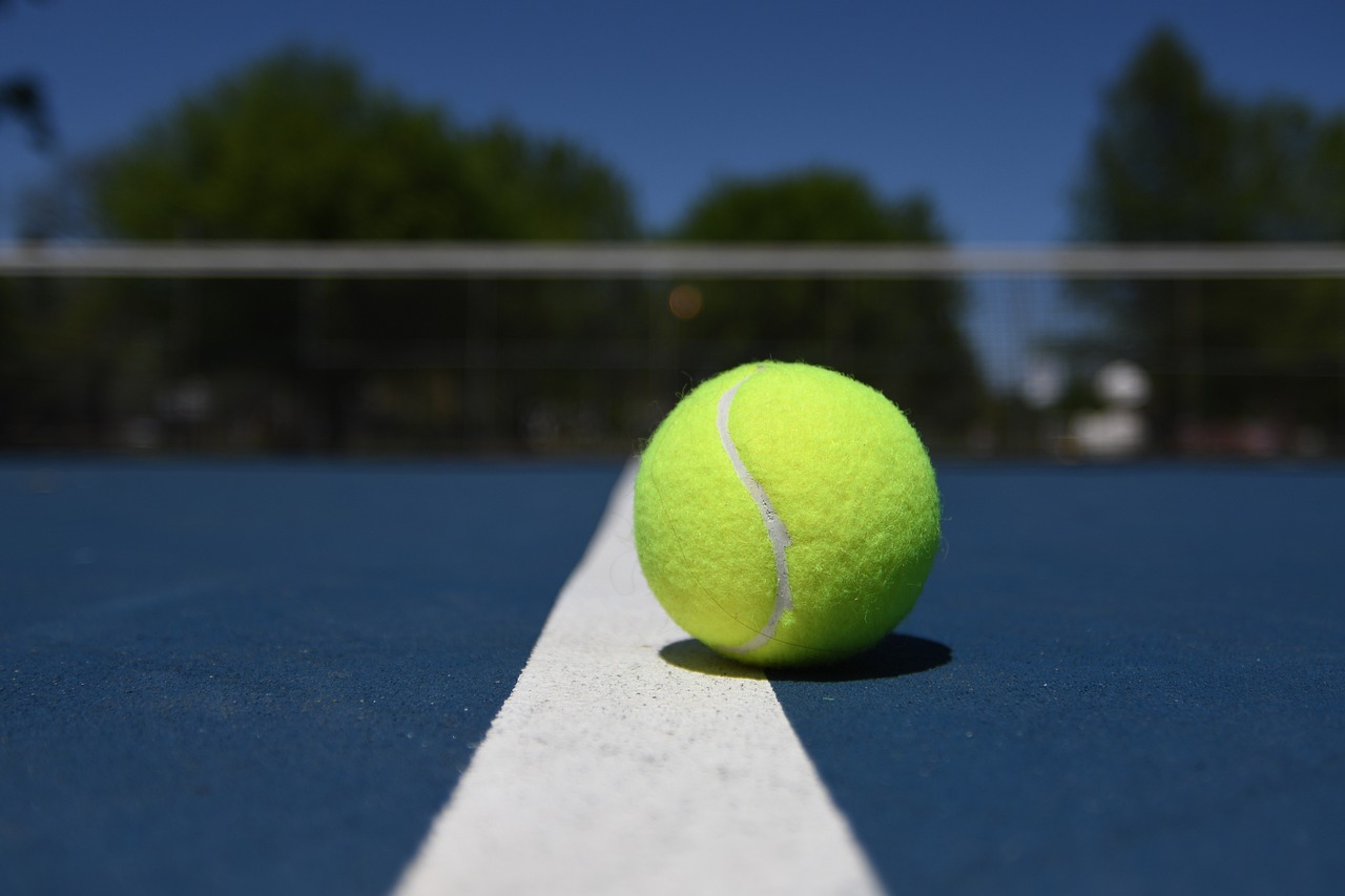 A tennis ball resting on the white line of a tennis court.