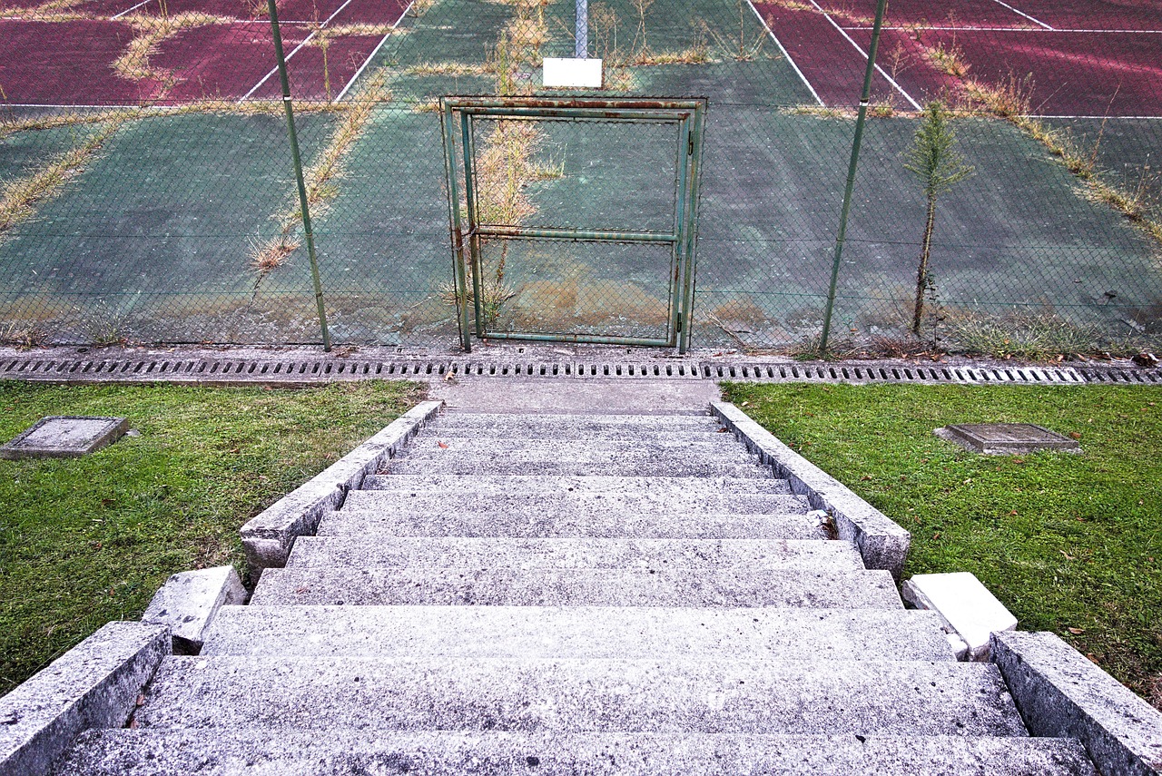 Concrete steps leading down to a fenced tennis court.