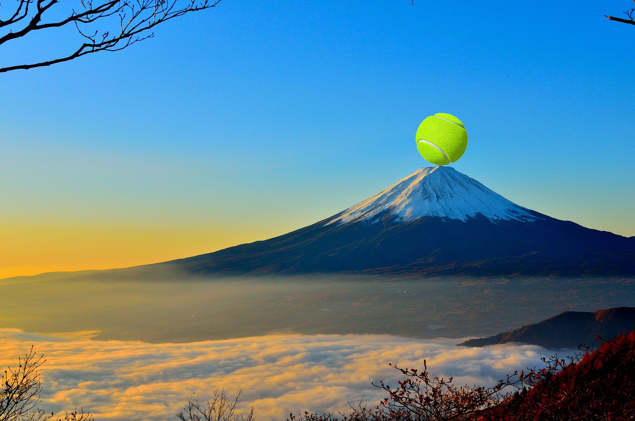 A tennis ball appears to be balanced on a mountain peak at sunset.