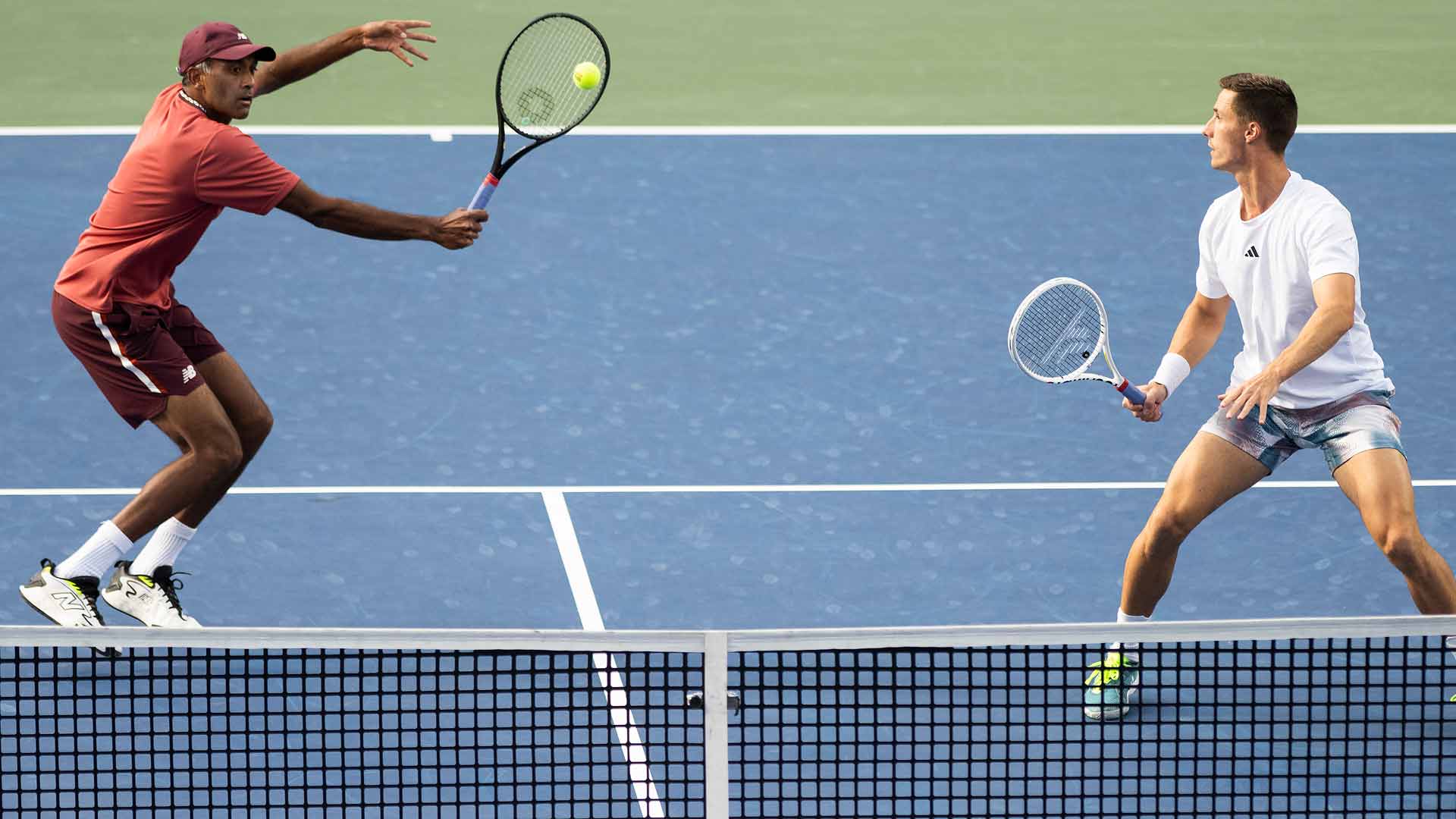 Two tennis players about to hit the ball over the net on a blue court.