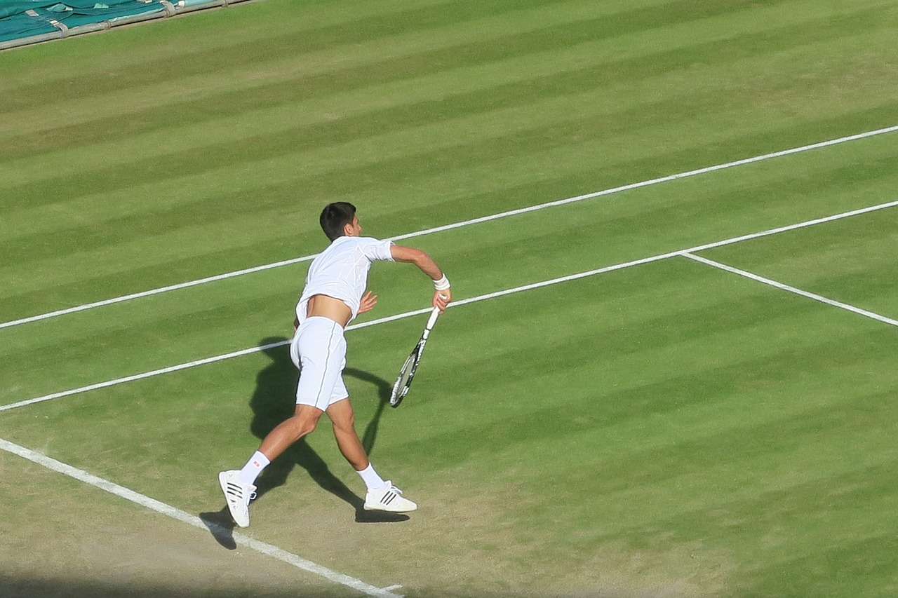 Male tennis player running on grass court preparing to hit the ball.